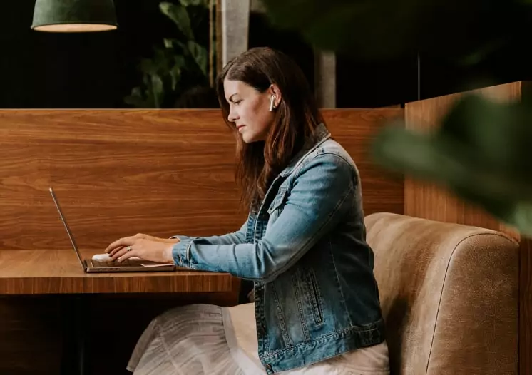 A woman working on her laptop in a cafe, managing digital marketing campaigns for a branding agency.